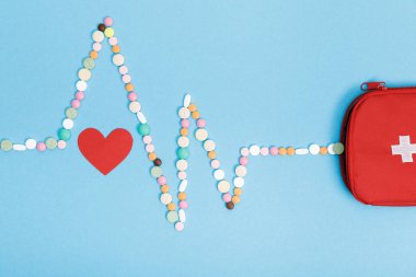 Flat lay with pills, first aid kit bag and paper heart on blue surface