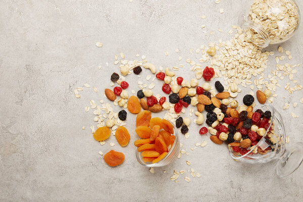 top view of oat flakes, dried apricots and berries, nuts messy scattered on textured grey surface 