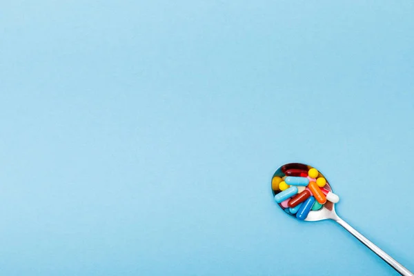 青い表面のカラフルな丸薬とスプーンのトップビュー — ストック写真