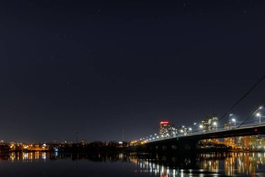 Işıklı binalar, köprü ve nehir geceleri ile karanlık Cityscape