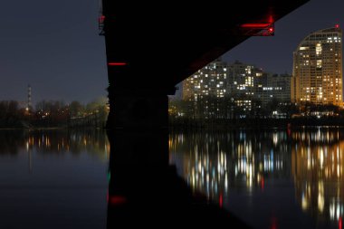 gece kıyısında sakin nehir ve aydınlatılmış evlerin üzerinde köprü ile karanlık Cityscape