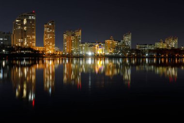 dark cityscape with illuminated buildings with reflection on water at night clipart