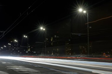 long exposure of lights on road at night near illuminated buildings clipart