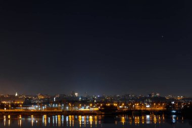 Işıklı binalar ve geceleri nehirde yansıma ile karanlık ve sakin bir şehir manzarası