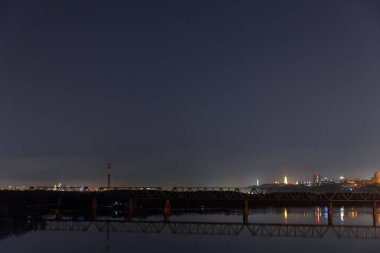 dark cityscape with calm river and bridge at night