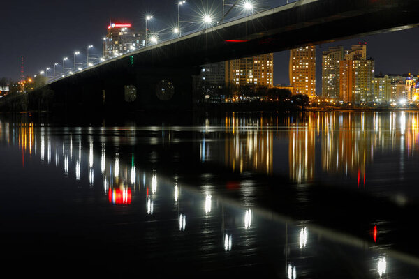 dark cityscape with illuminated bridge and reflection on river at night
