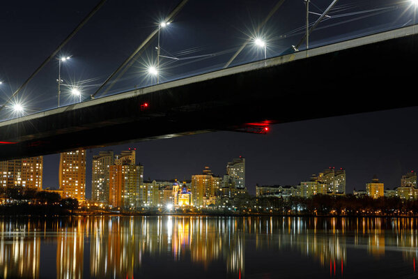 dark cityscape with bridge, reflection on river and illuminated houses at night