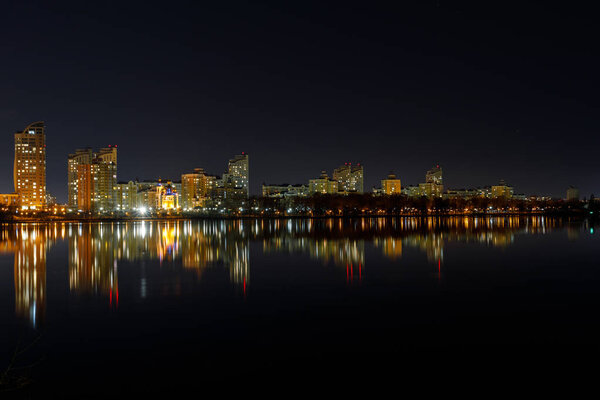 picturesque dark cityscape with illuminated buildings, river and night sky