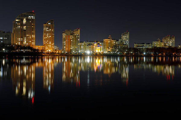 dark cityscape with illuminated buildings with reflection on water at night