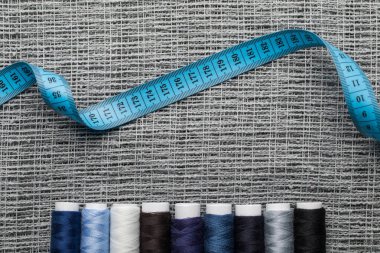top view of blue and grey thread coils with measuring tape on sackcloth  clipart