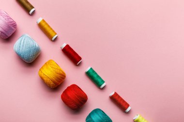 top view of colorful knitting yarn balls and thread coils on pink with copy space clipart