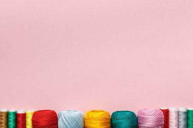 top view of arranged colorful cotton knitting yarn balls and thread coils isolated on pink with copy space clipart
