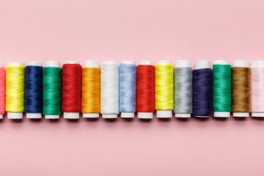top view of colorful thread coils in row on pink clipart
