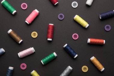 top view of colorful thread coils with various buttons isolated on black clipart