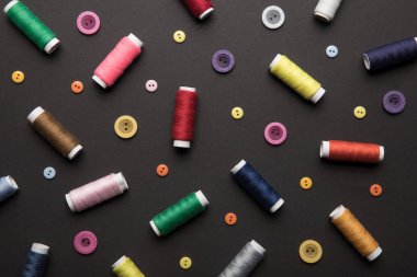 top view of colorful thread coils with various buttons isolated on black clipart