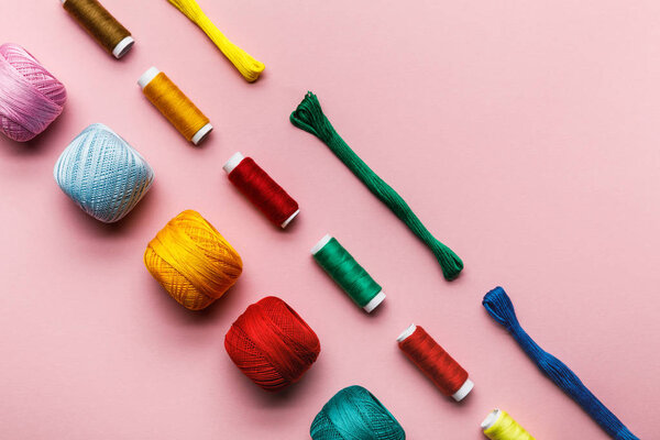 top view of colorful knitting yarn balls, embroidery threads and thread coils on pink 