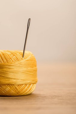 selective focus of yellow cotton knitting yarn ball with needle isolated on beige with copy space clipart