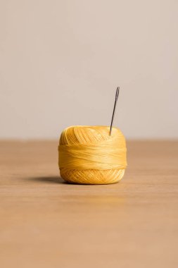 selective focus of yellow cotton knitting yarn ball with needle isolated on beige clipart