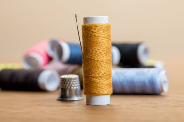 selective focus of cotton thread coil with needle isolated on beige clipart