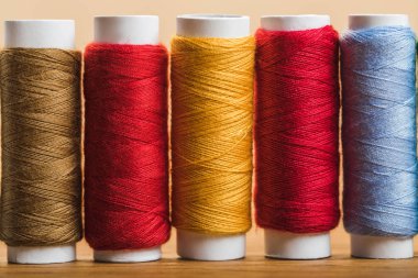 close up view of colorful cotton thread coils in row isolated on beige clipart