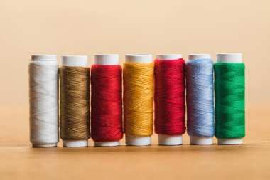 colorful cotton thread coils in row on wooden table isolated on beige clipart