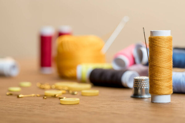 selective focus of thread coil with clothing buttons on wooden table isolated on beige