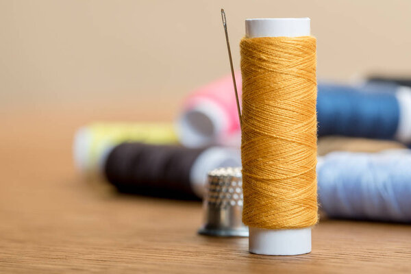 selective focus of thread coil with needle on table isolated on beige with copy space
