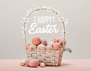 wicker basket with pink painted eggs, flowers and happy Easter lettering on grey background clipart