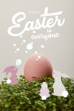 pink painted chicken egg on green grass with happy Easter to everyone lettering and rabbits illustration clipart