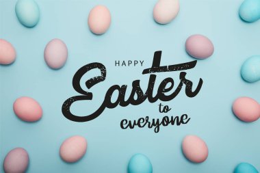 top view of painted multicolored eggs on blue background with happy Easter to everyone lettering clipart