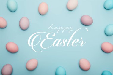 Mutlu Paskalya yazısı ile mavi arka planda boyalı yumurtaların üst görünümü