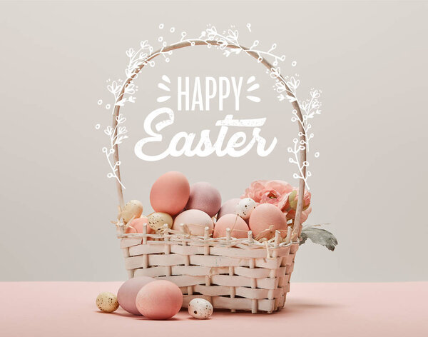 wicker basket with pink painted eggs, flowers and happy Easter lettering on grey background