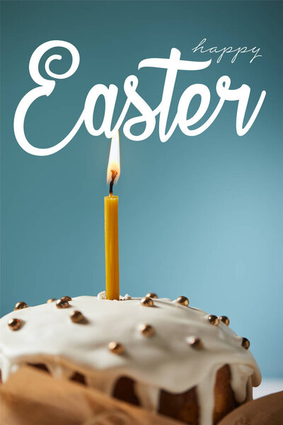 close up of traditional Easter cake with burning candle and white sprinkles on blue background with happy easter lettering