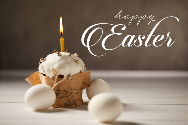 traditional Easter cake with burning candle and white chicken eggs on brown background with happy easter lettering