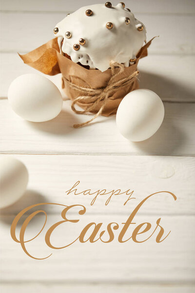 traditional Easter cake and chicken eggs on white wooden table with happy easter lettering