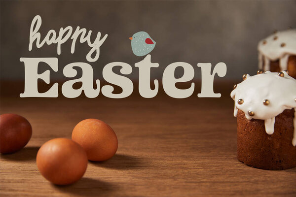 selective focus of traditional Easter cakes and chicken eggs on wooden table with happy easter lettering and bird illustration