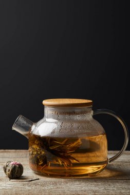 kopya alanı ile siyah izole ahşap masa üzerinde çiçek açan çay ve çay topları ile şeffaf çaydanlık