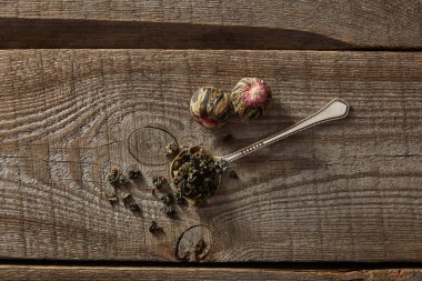 top view of spoon with green tea and blooming tea balls on wooden table clipart