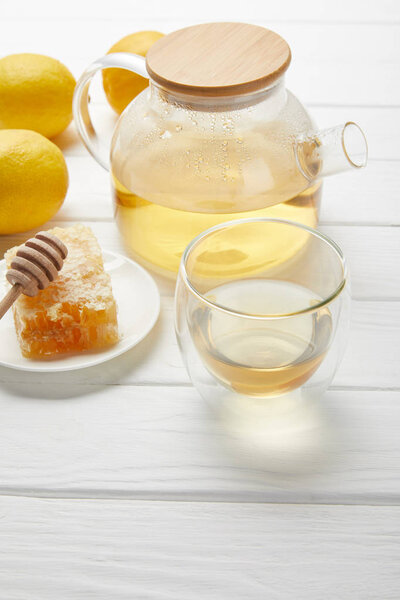 teapot with organic herbal tea, glass, lemons and honeycomb on white wooden table