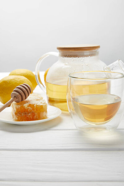 teapot with organic herbal tea, glass, lemons and honeycomb on white wooden table 