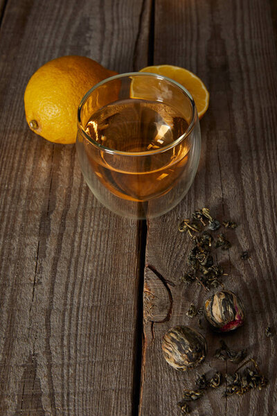 glass of traditional chinese blooming tea, lemons and tea balls on wooden table 