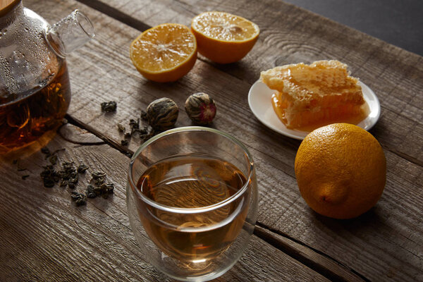transparent teapot with glass of chinese blooming tea, honeycomb, tea balls and lemons on wooden table