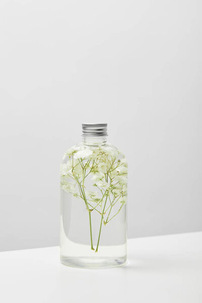 organic cosmetic product in transparent bottle with herbs on white table isolated on grey 