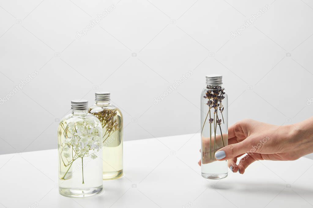 partial view of woman holding bottle with organic lotion on white table