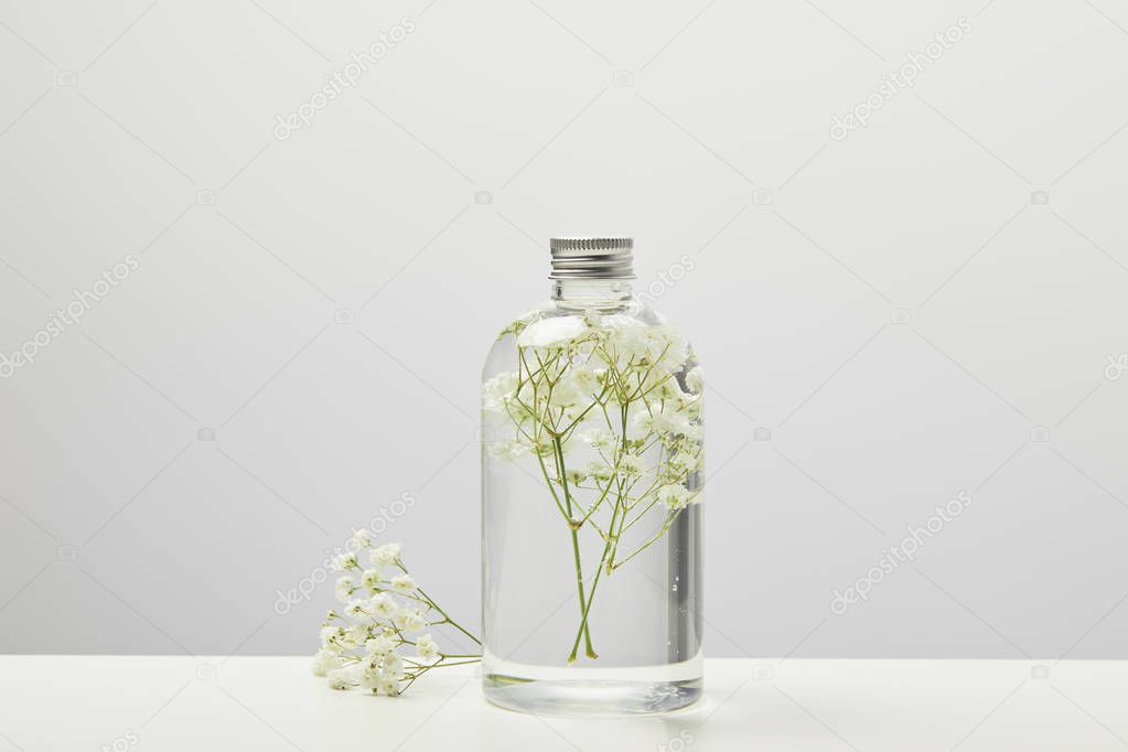 natural homemade beauty product with white wildflowers in transparent bottle on grey background