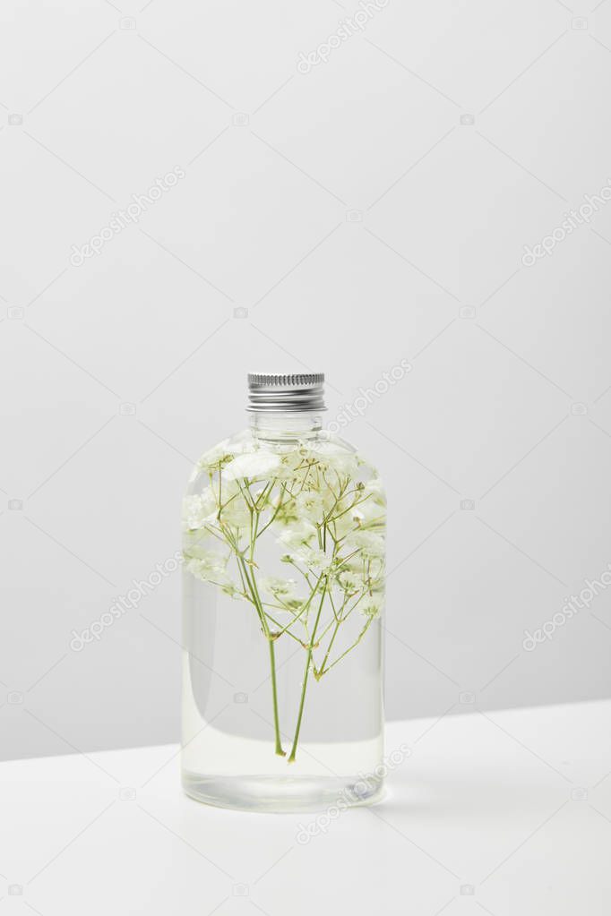 organic cosmetic product in transparent bottle with herbs on white table isolated on grey 