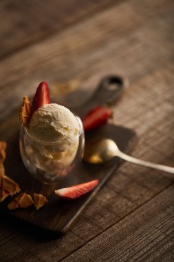 selective focus of delicious ice cream with strawberries in glass and spoon on wooden table clipart