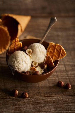 ahşap masada kase de waffle, kaşık ve fındık parçaları ile lezzetli dondurma