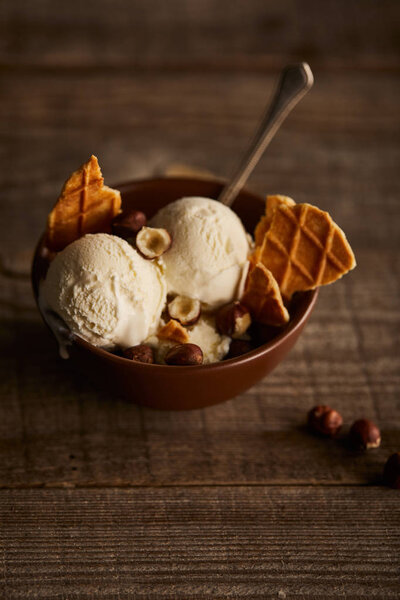 delicious ice cream with pieces of waffle and hazelnuts in bowl on wooden surface