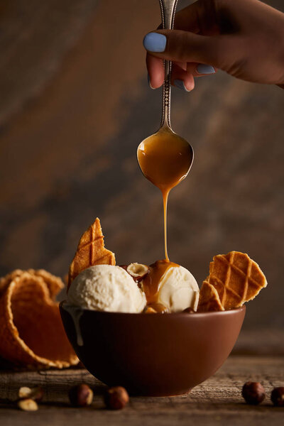 Cropped view of woman pouring caramel on delicious ice cream with pieces of waffle